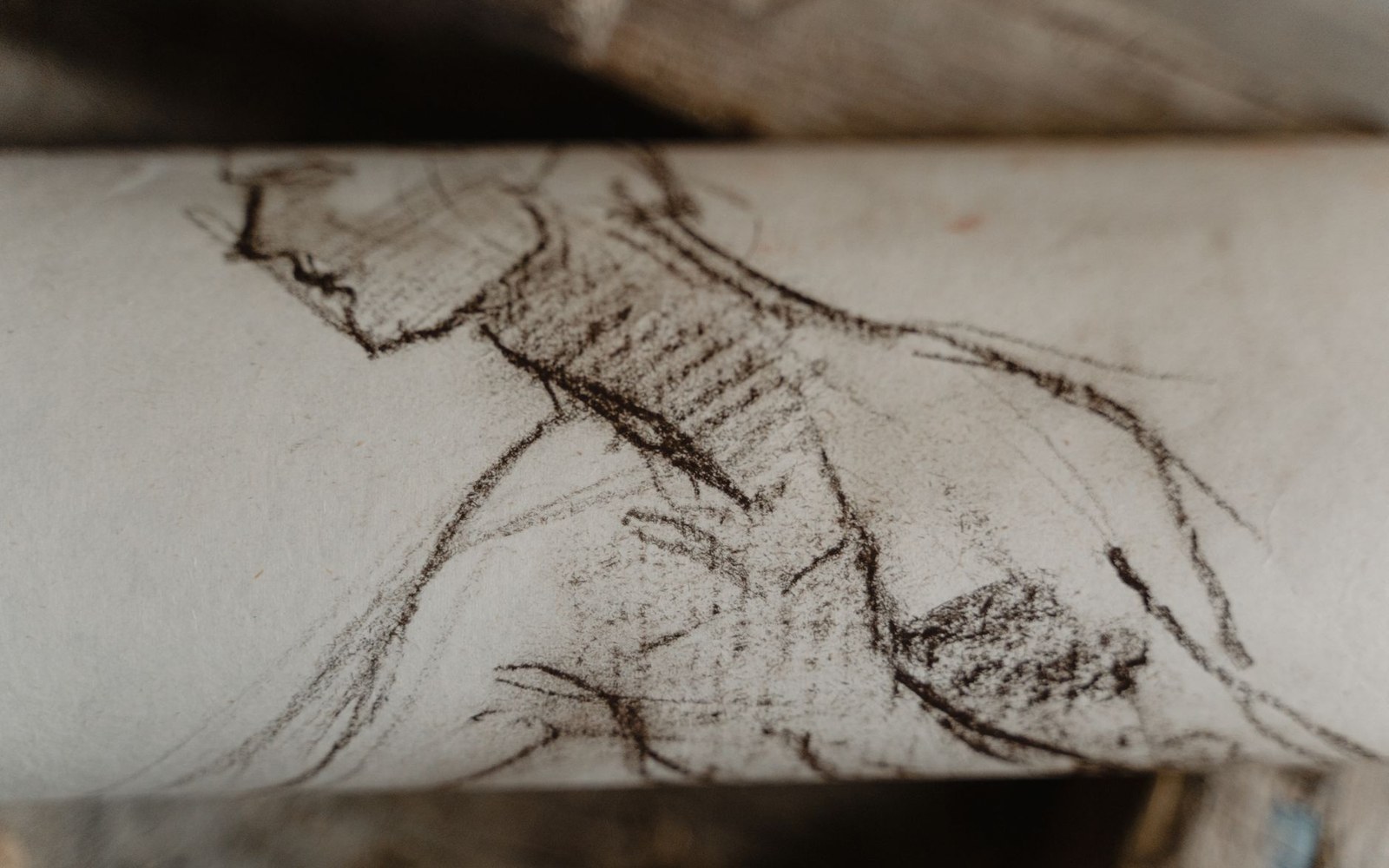 Charcoal figure sketch on a rolled sheet of paper showing a hunched torso and arm