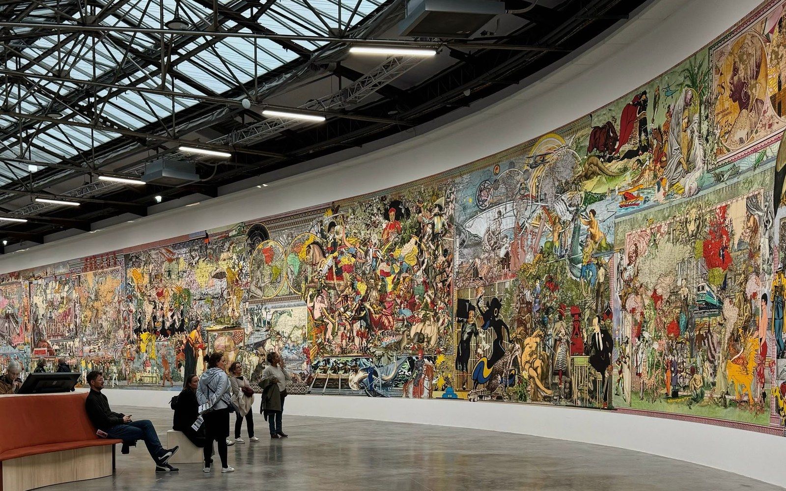 Visitors view a sprawling, densely illustrated mural along a curved gallery wall