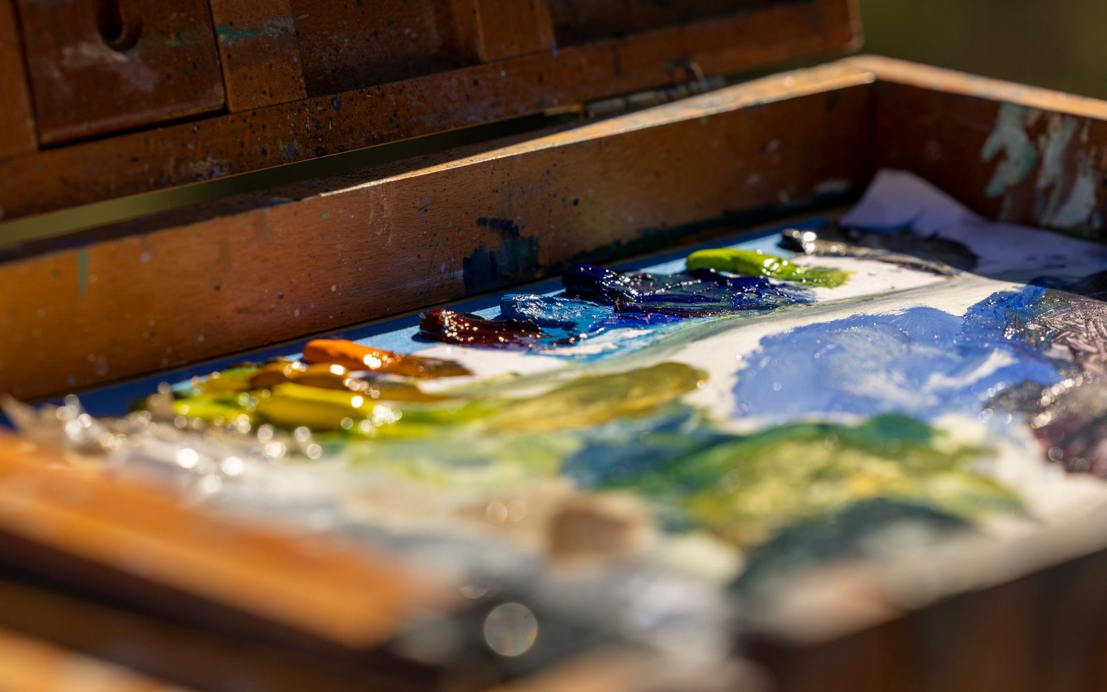 Blobs of oil paint in various colors mixed on a wooden artist's palette box