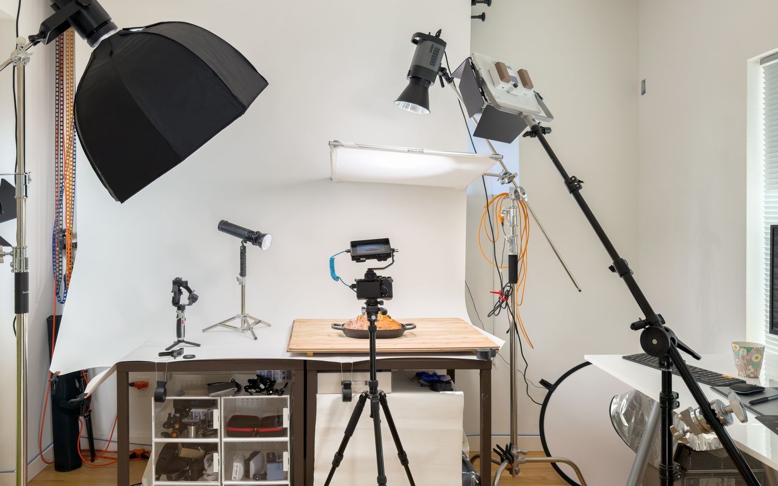 A camera on a tripod aims at a plated dish surrounded by studio lighting equipment
