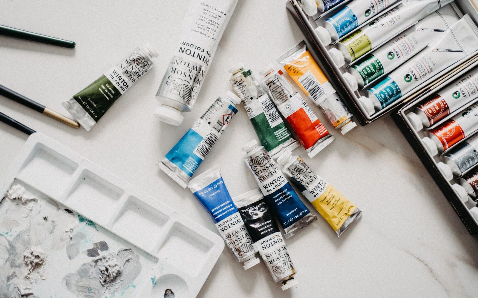 A Winsor & Newton oil colour tin and a Kolinsky sable brush resting on a paint-crusted wooden table